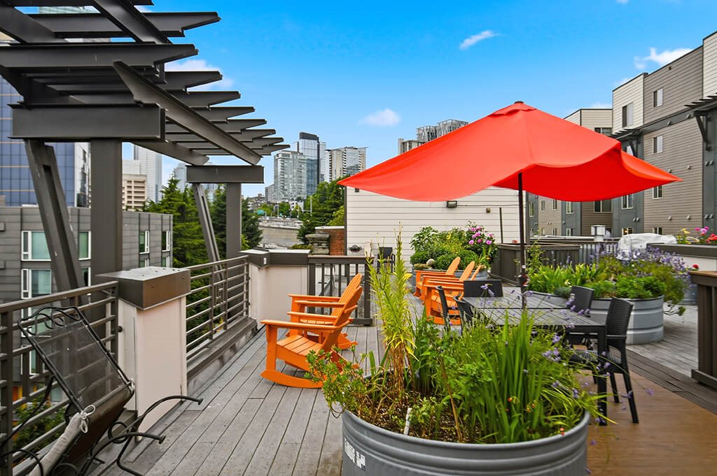 A red umbrella is on a wooden deck with a metal planter.